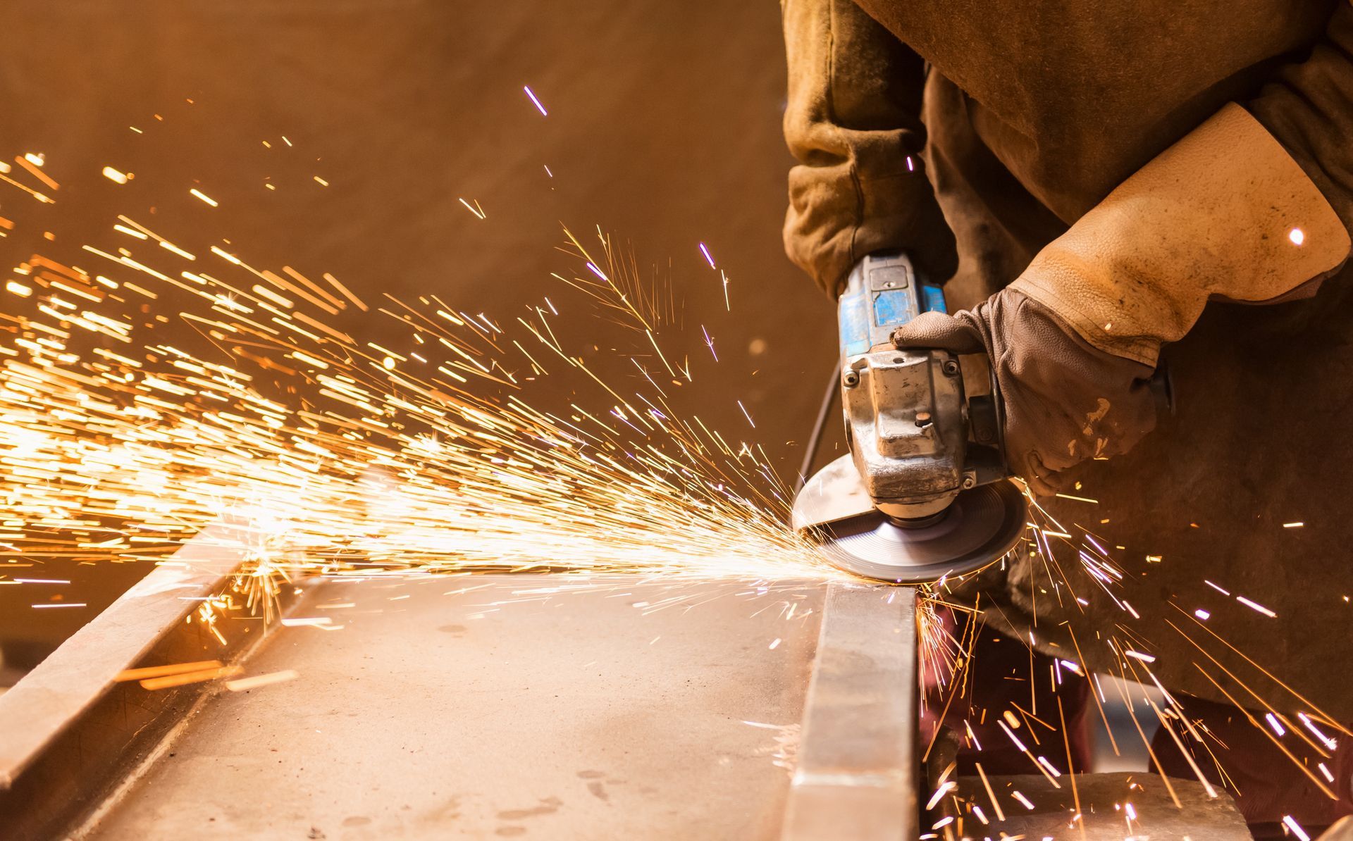A worker using a grinding wheel, creating sparks, wearing gloves.