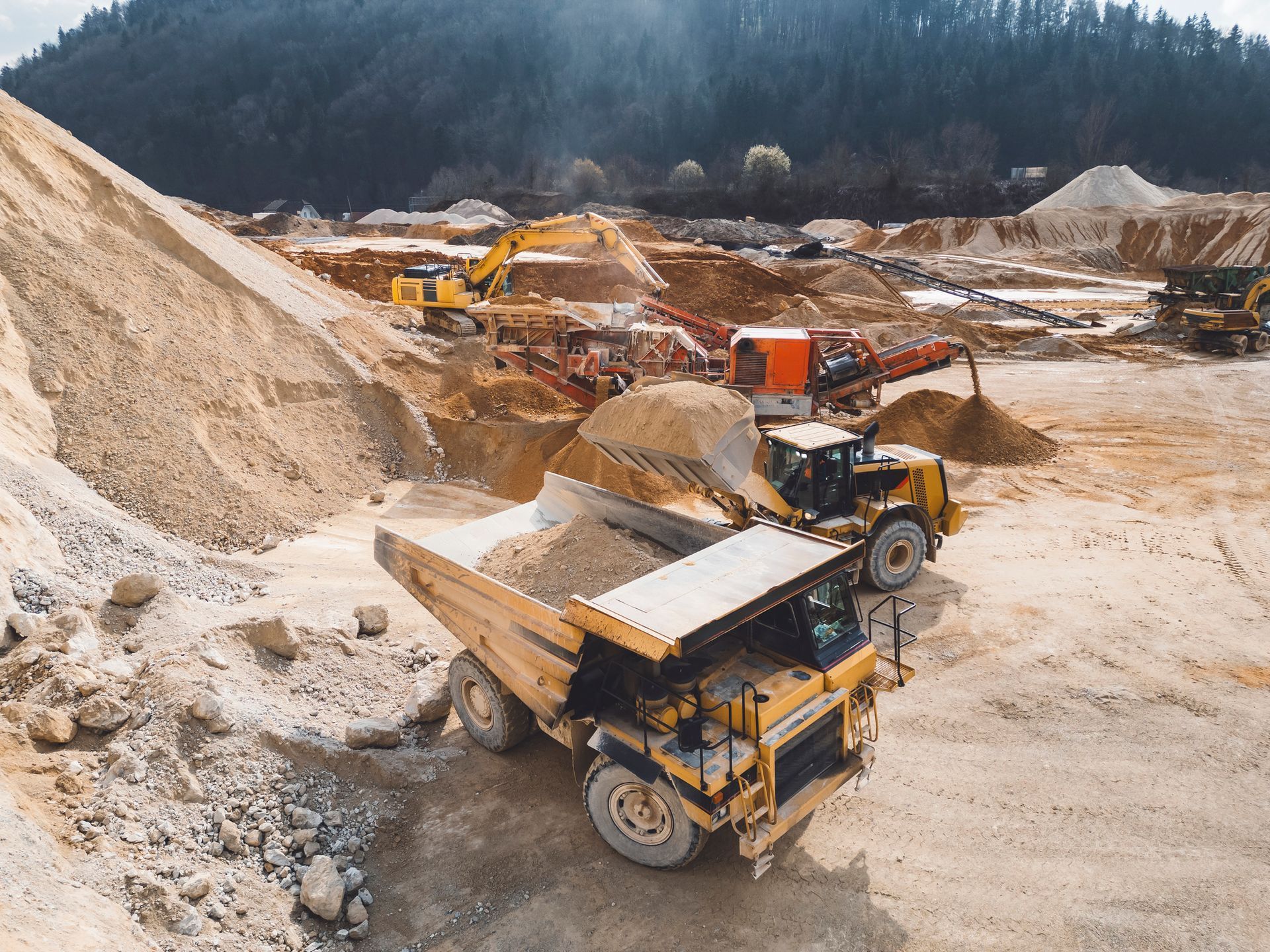 Dump truck being loaded with gravel at a quarry, other heavy machinery visible, bright sunlight. Dump truck being loaded with gravel at a quarry, other heavy machinery visible, bright sunlight.