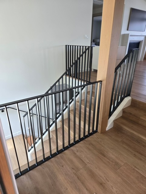 Interior staircase with black metal railings, light wood steps and flooring, and white walls.