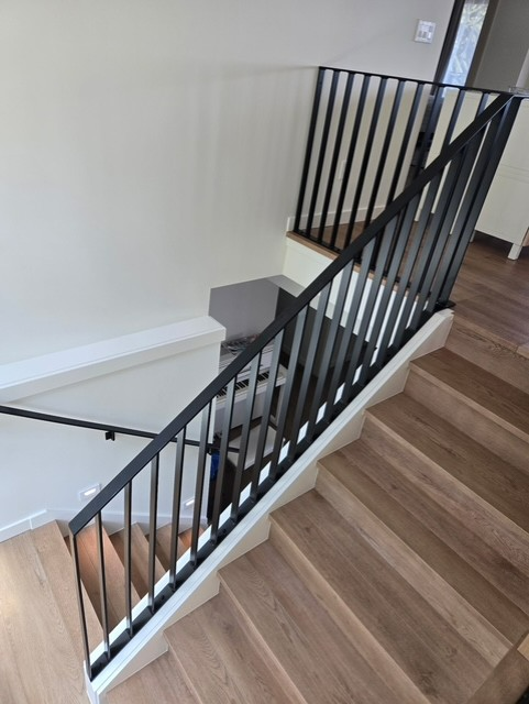 Staircase with wooden steps and black metal railing, white trim, viewed from above.