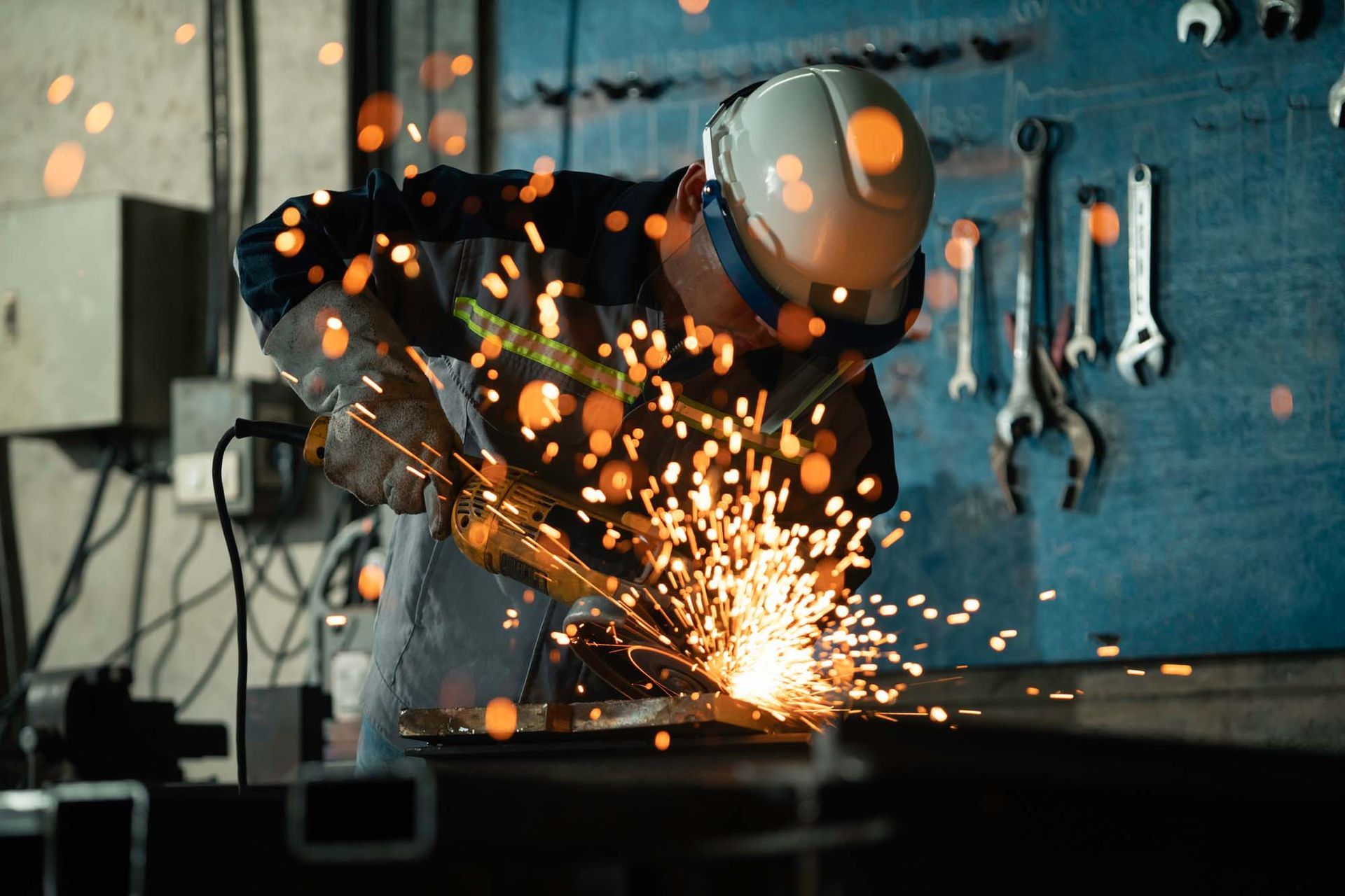 Structural Welder cutting metal with power tool as sparks fly in industrial workshop setting.