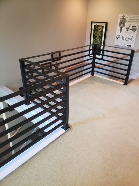 Black metal railing surrounding a second-floor landing with art and beige carpet.