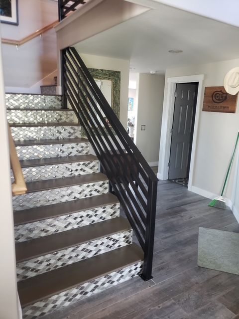 Staircase with modern black railing and mosaic tile steps in a home.