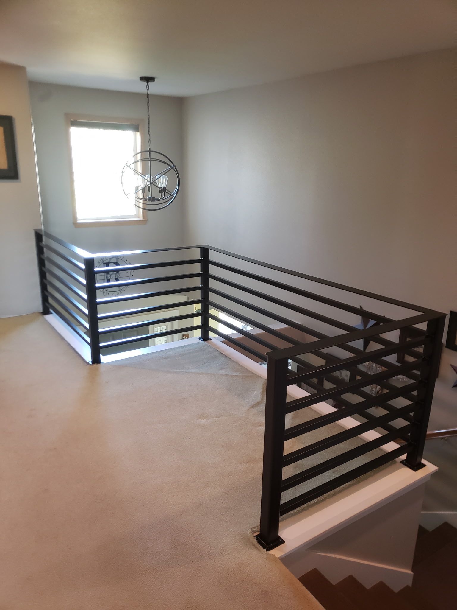 Interior view of a second-story landing with black horizontal railing and white base.