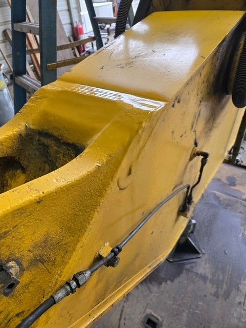 Yellow industrial machine component, close-up. Dirty and well-used, with hydraulic lines attached.