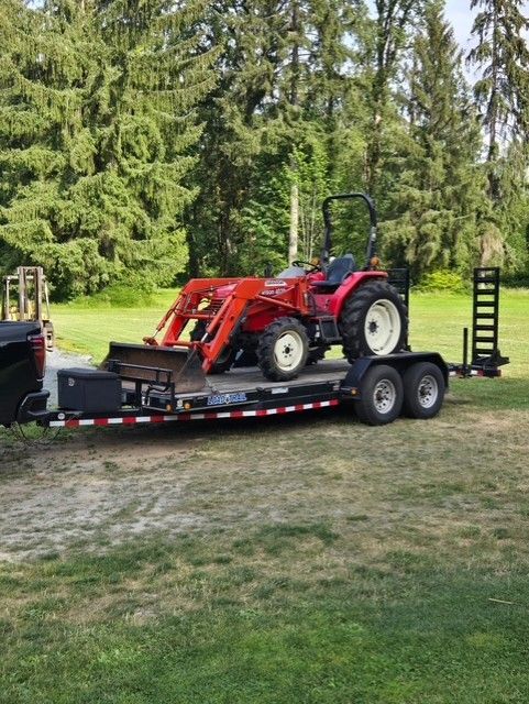 Red tractor on a trailer, parked on grass. Trees in the background.