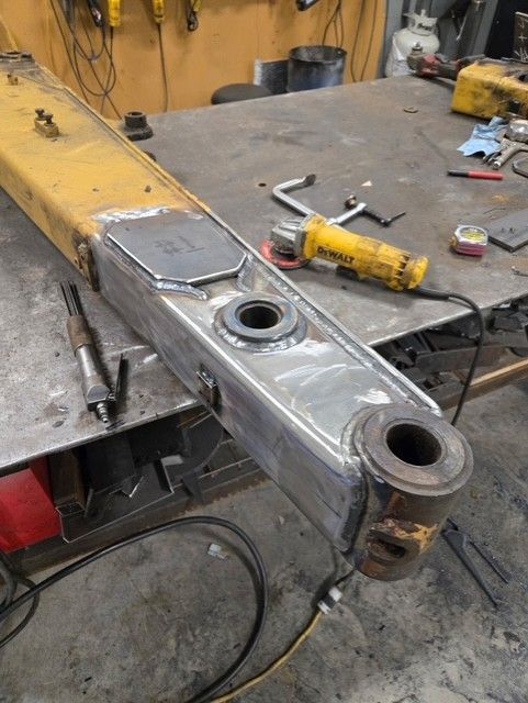 Yellow and silver arm being repaired with welds, metal grinding tools, on a workbench.