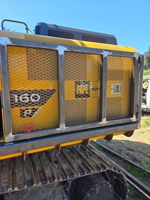 Yellow excavator with a protective metal grill on its side, outdoors.