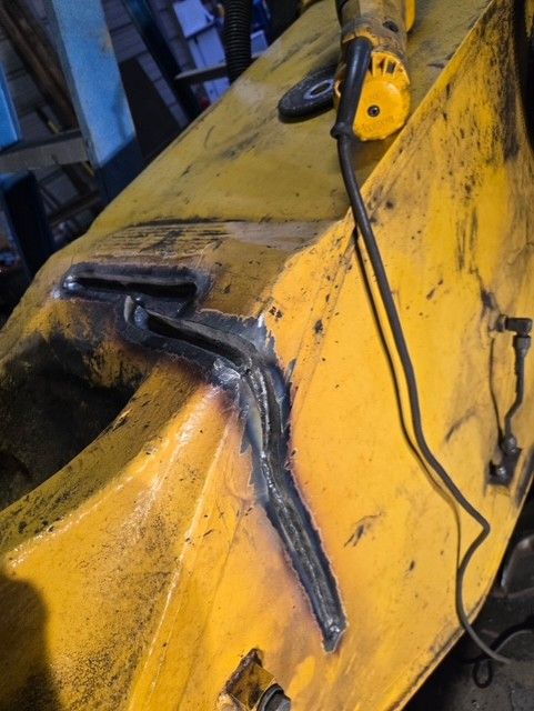 Yellow metal object with weld repairs, an angle grinder sits nearby.