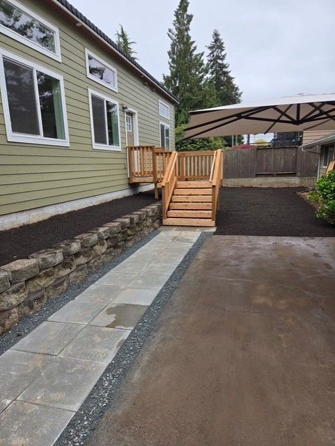 Pathway leading to a wooden deck with stairs next to a building. Gravel and mulch surround the path.