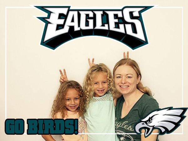 A woman and two little girls are posing for a picture in front of an eagles logo.