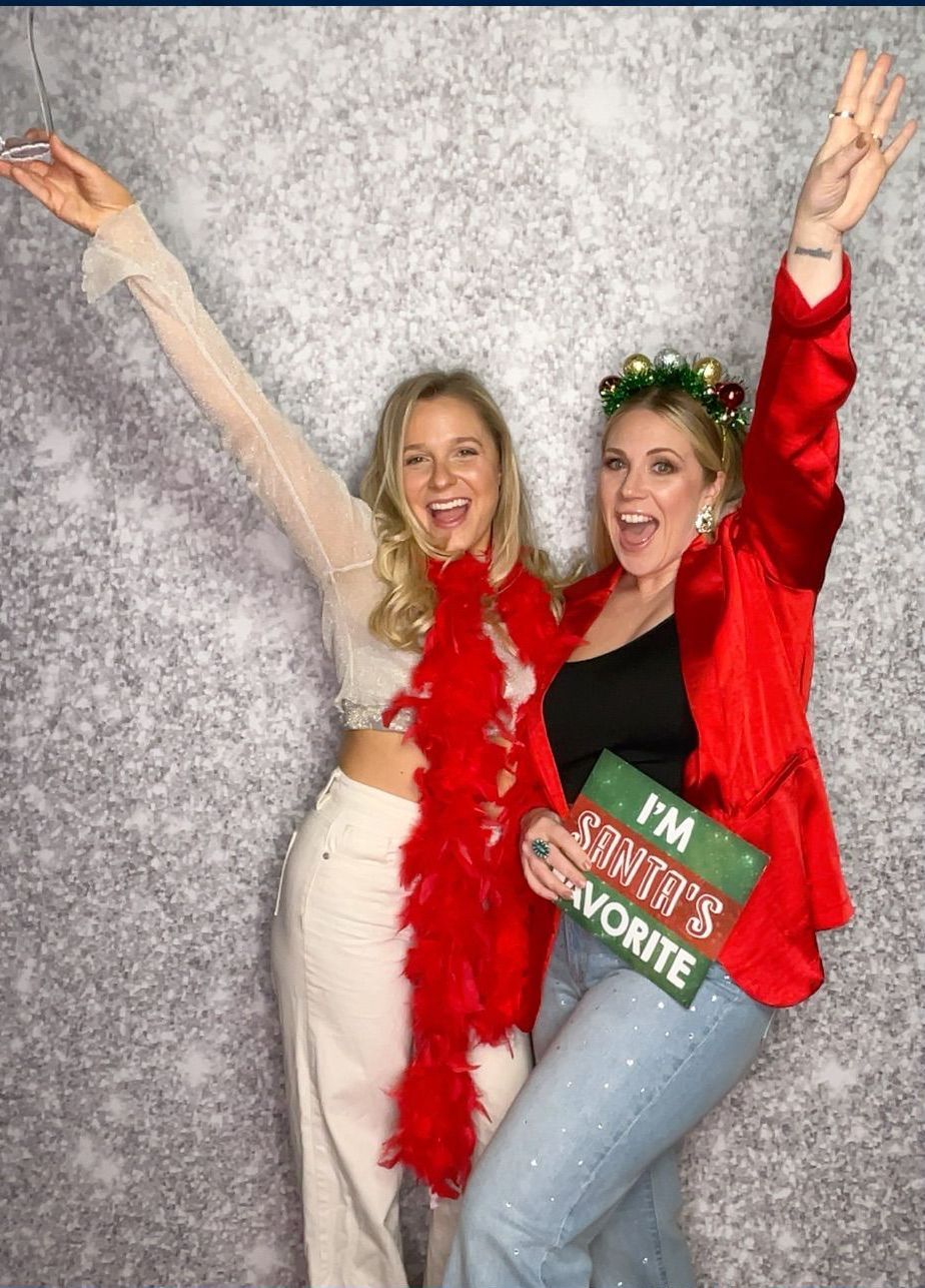 Two bestfriends posing for a picture in a photo booth at holiday party.