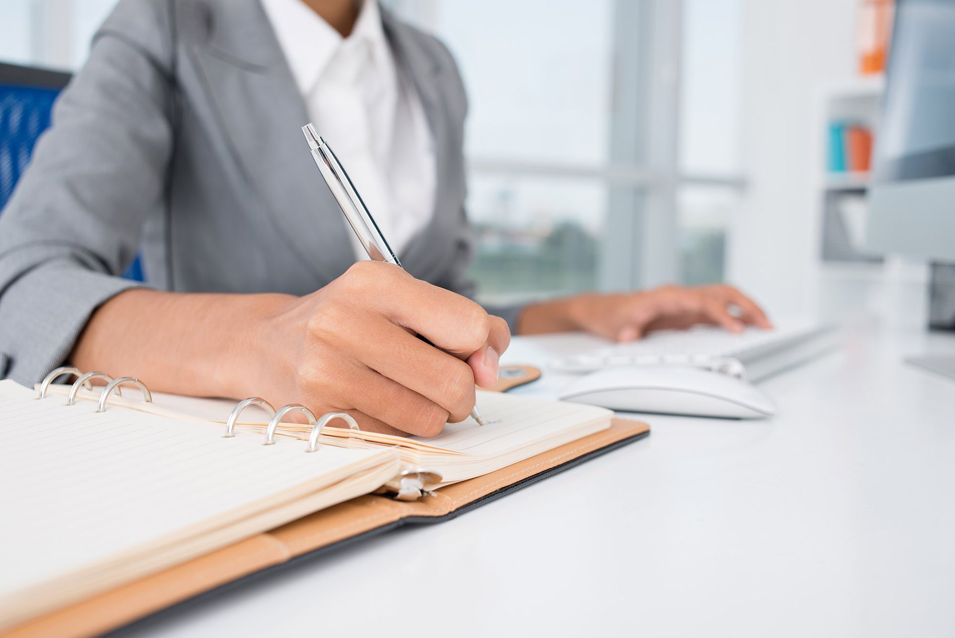 Person writing in a notebook at a desk. Close-up of hands holding a pen, taking notes.