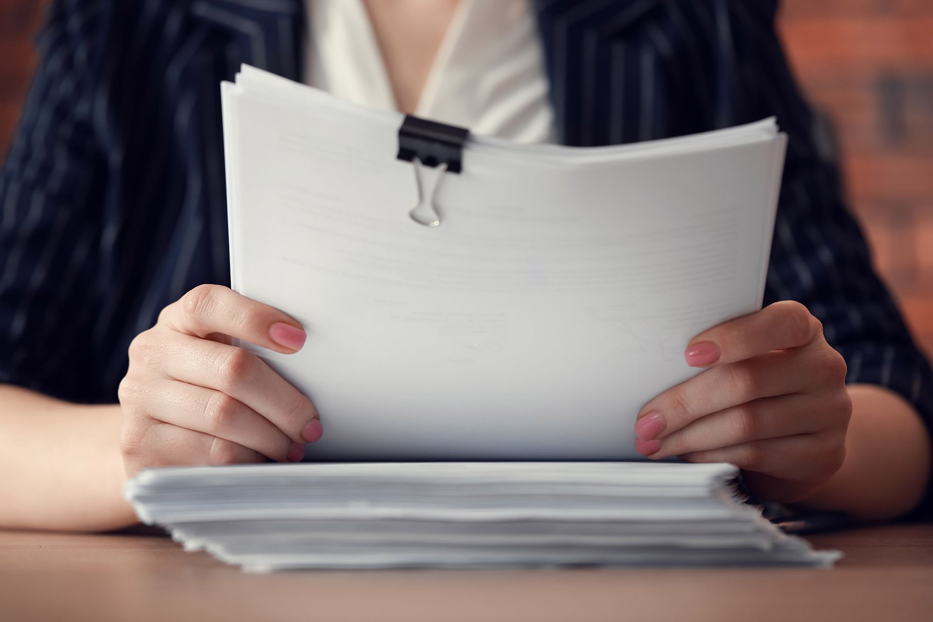 Woman holding a stack of papers, secured with a black clip, on a desk.