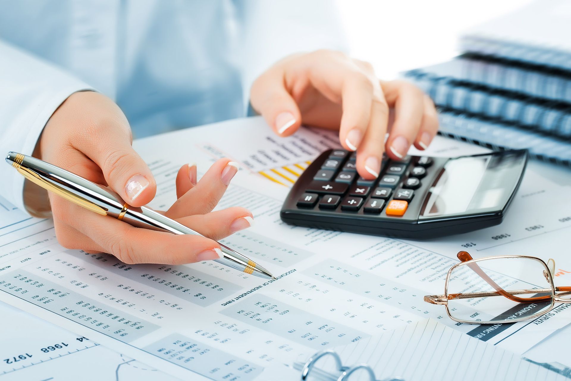 Hands using a calculator and pen on financial documents with eyeglasses.