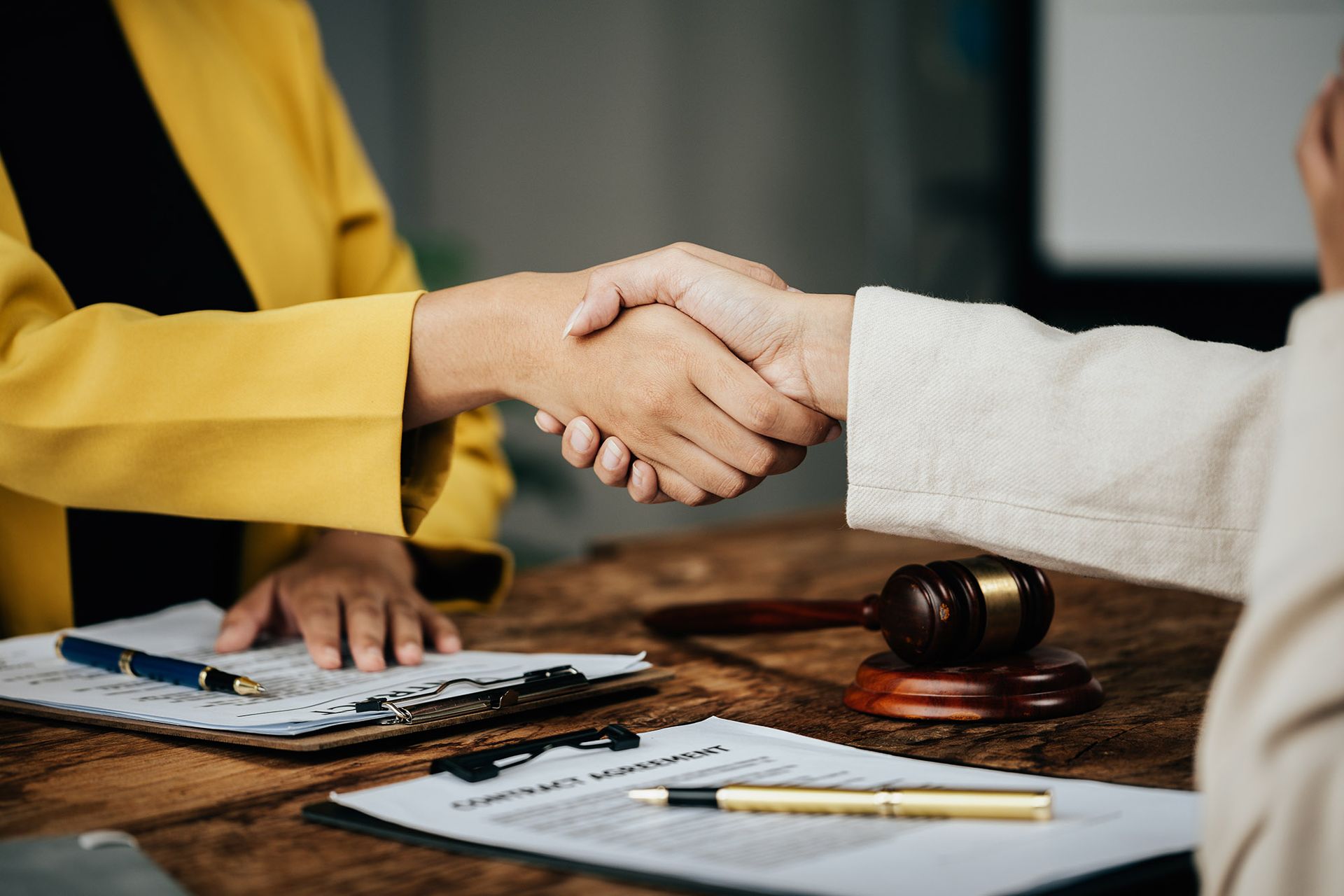 Two people shaking hands over a table with documents and a gavel.