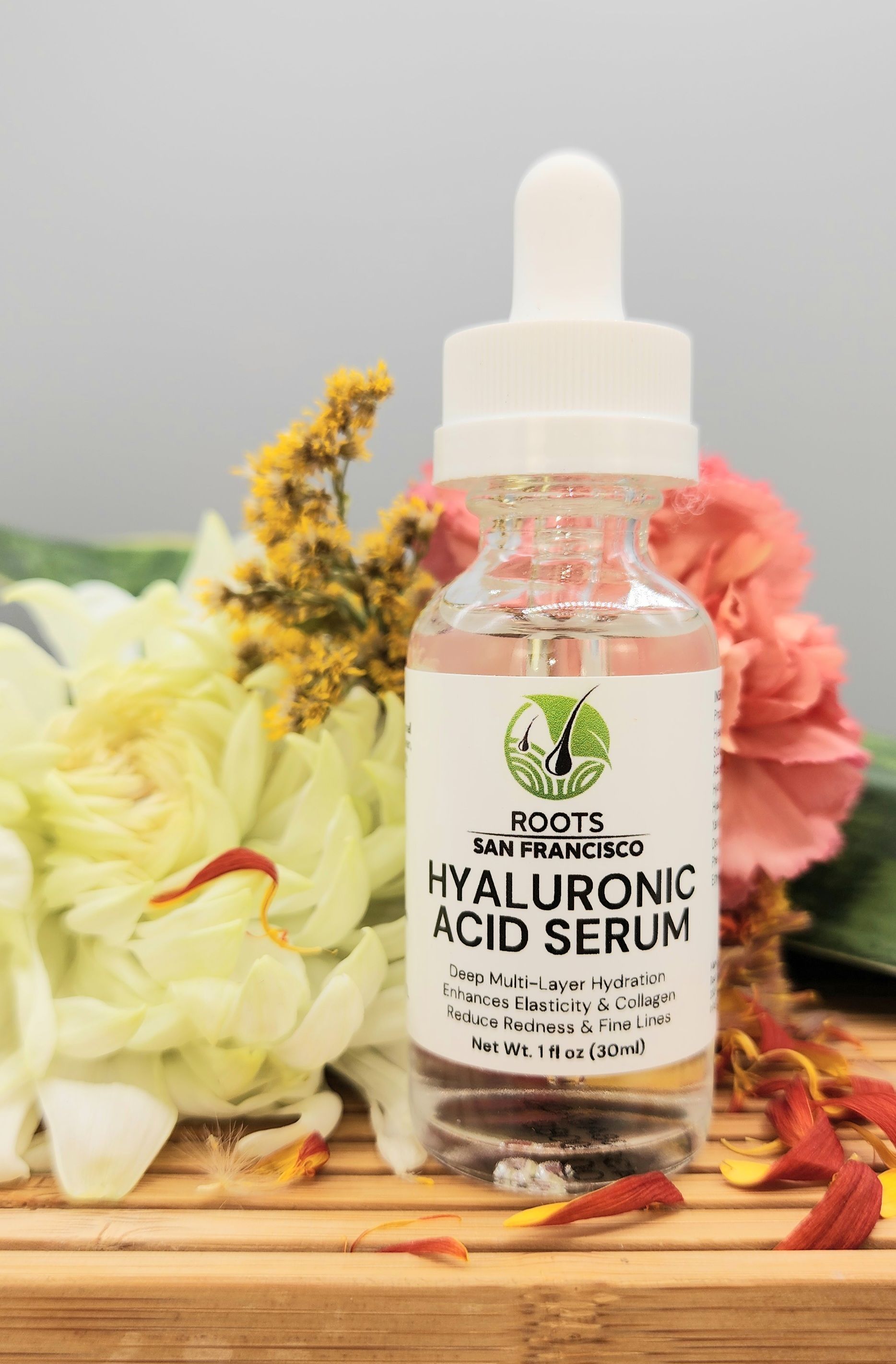 A bottle of hyaluronic acid serum is sitting on a wooden table next to flowers.