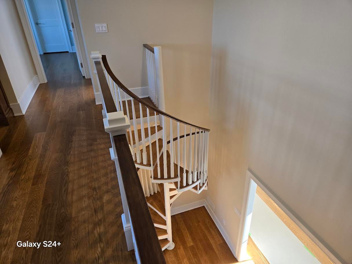 A wooden staircase with white railings descends from a hallway with hardwood floors into a lower level.