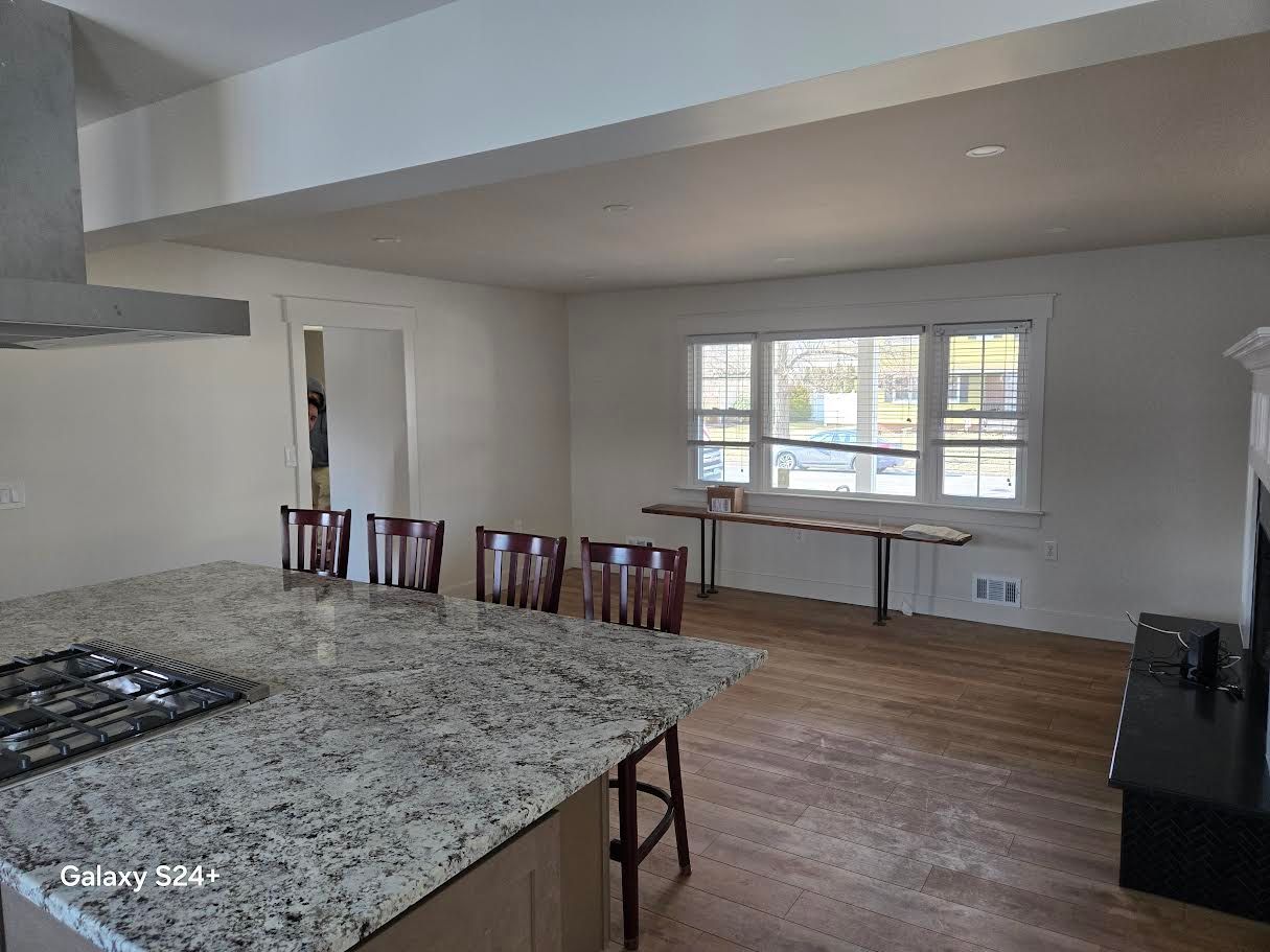 A kitchen island with a granite countertop sits in front of a dining area with a long table and four wooden chairs.