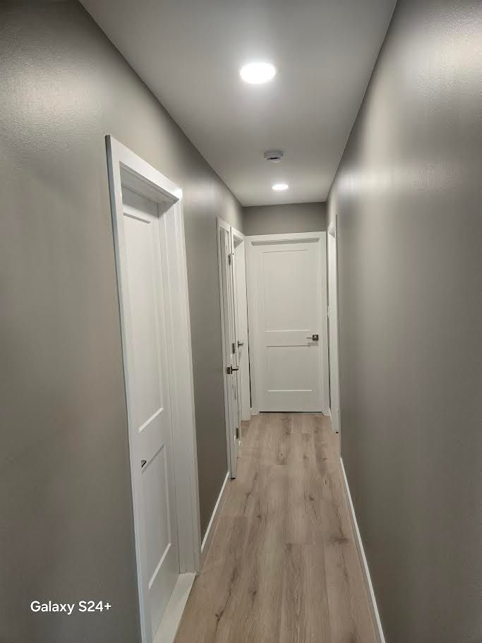 A brightly lit hallway with light wood floors, grey walls, and white doors leading to rooms.