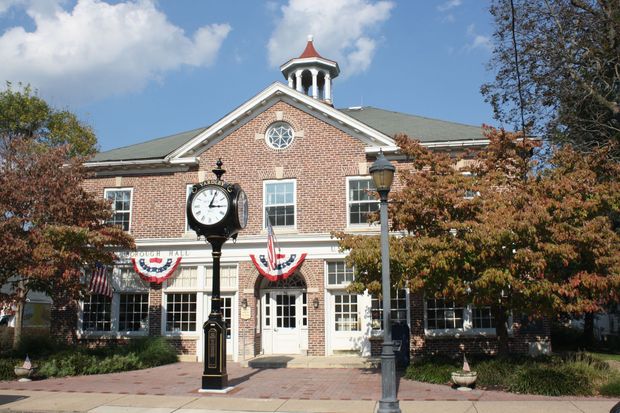 Brick building with clock, US flags, trees, and street lamp.
