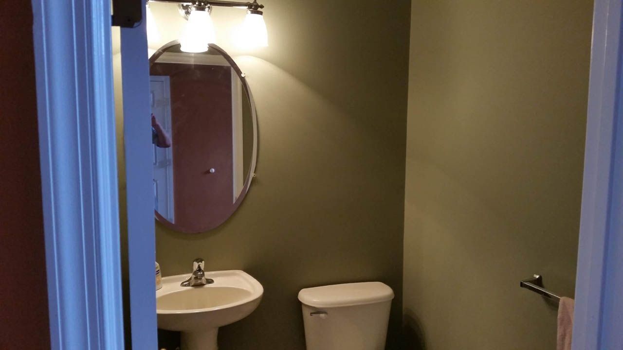 A small bathroom with olive green walls, oval mirror, and white sink and toilet.