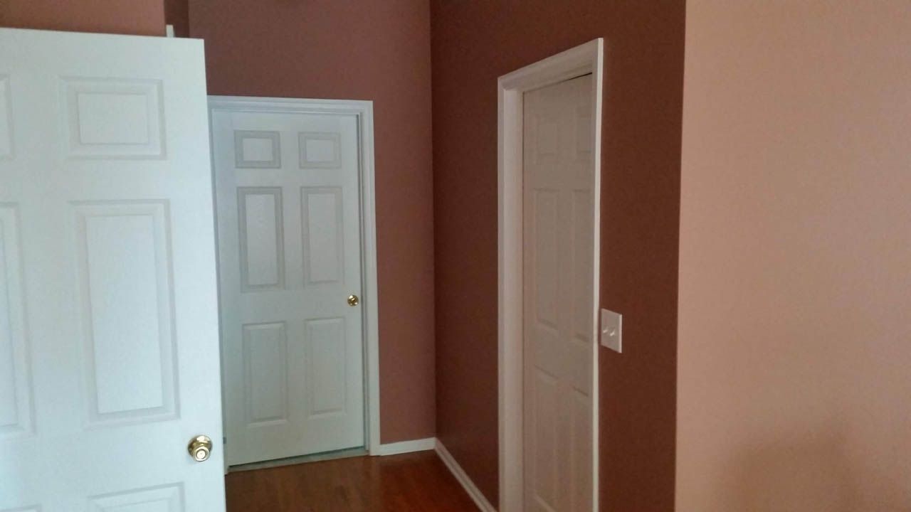 Interior view of a room with three white doors and brown and pink walls. Wooden floor.