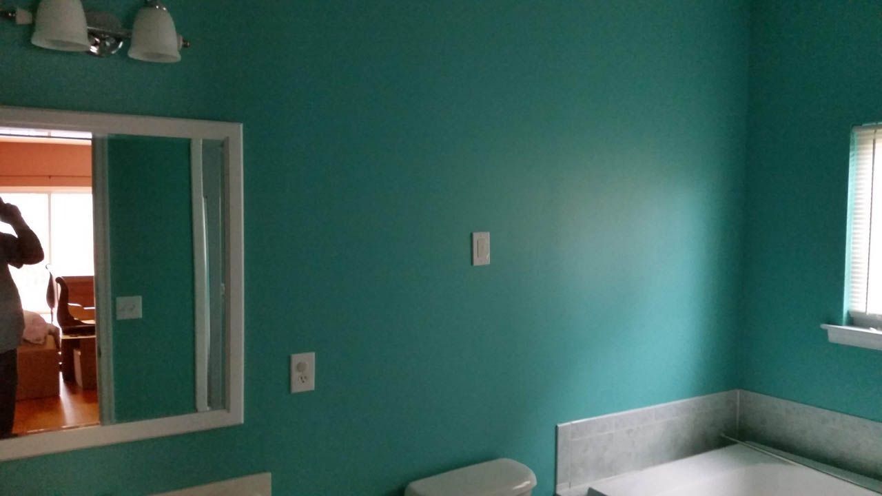 Bathroom with teal walls, white trim, and a built-in bathtub. A person is reflected in the mirror.