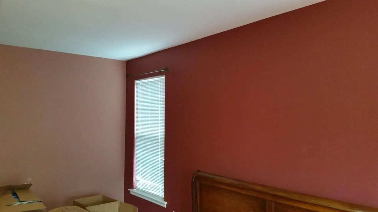 Bedroom walls painted two shades of red; white ceiling and window with blinds; wooden headboard.