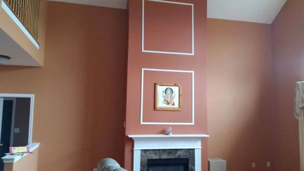 A tall orange wall with a fireplace and picture, with white trim and a loft area.