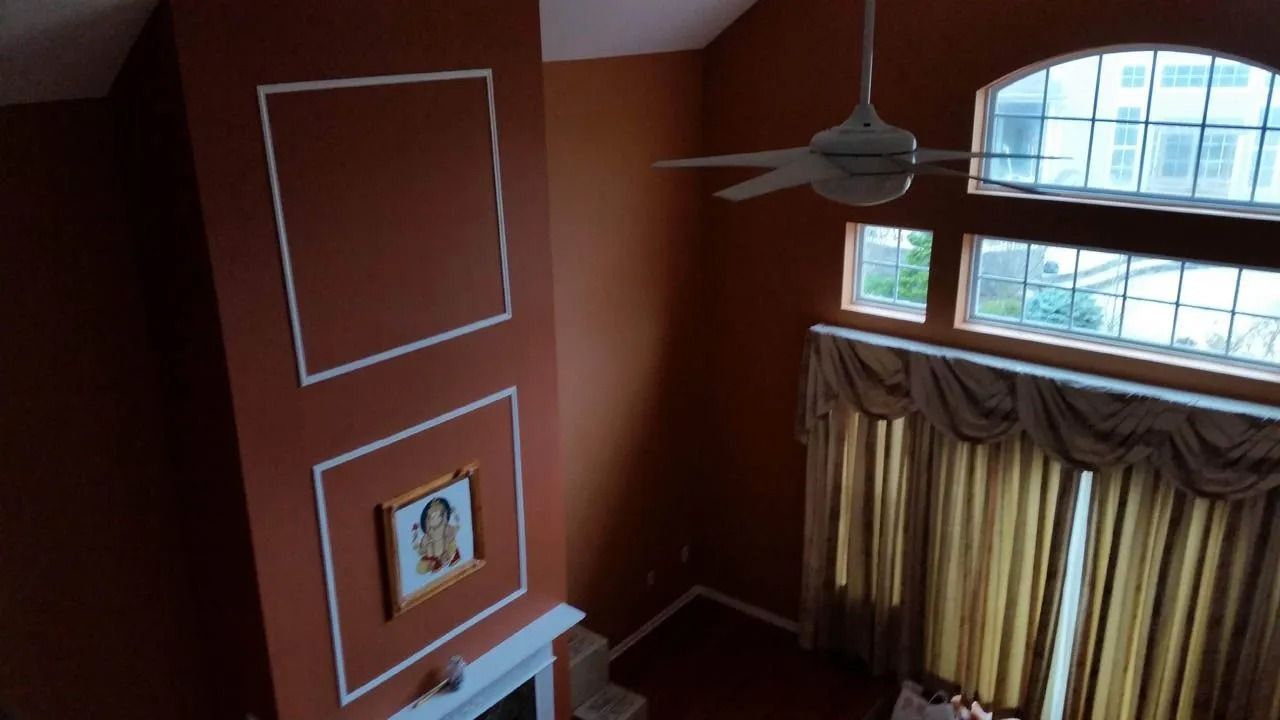 High-angle view of a room with orange walls, a fireplace, and large windows with gold curtains.