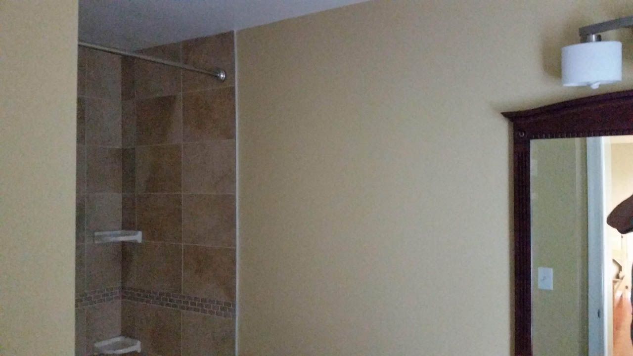 Bathroom interior with beige walls, tiled shower, mirror, and light fixture.