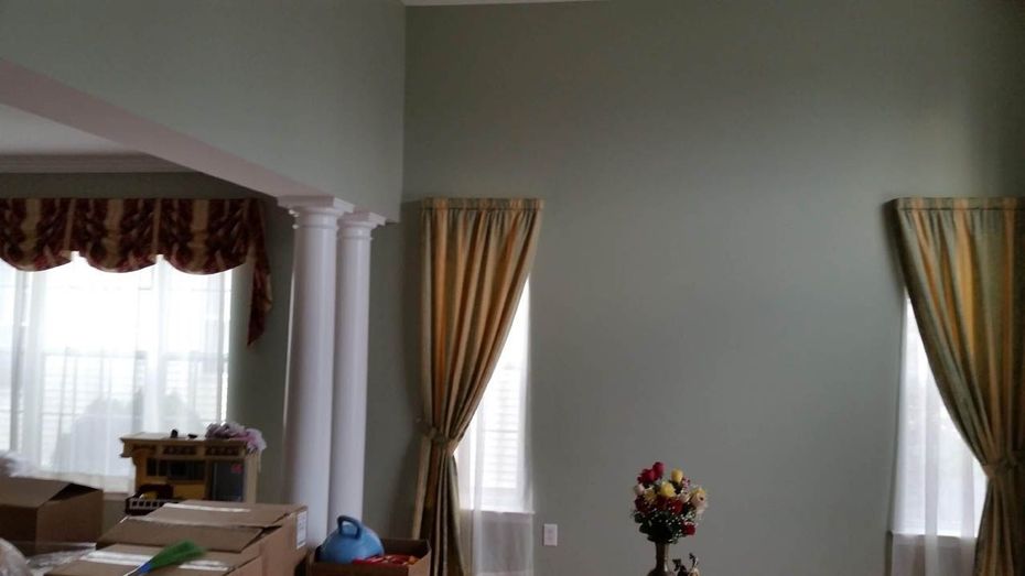 Living room with green walls, two tall windows with gold curtains, and a decorative flower arrangement.