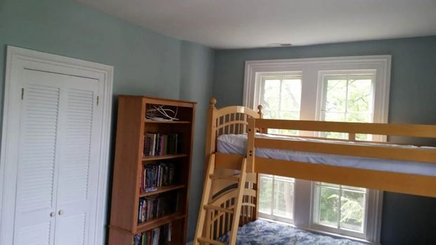 Bedroom with bunk bed, bookshelf, and closet. Blue walls, white trim, natural wood furniture.