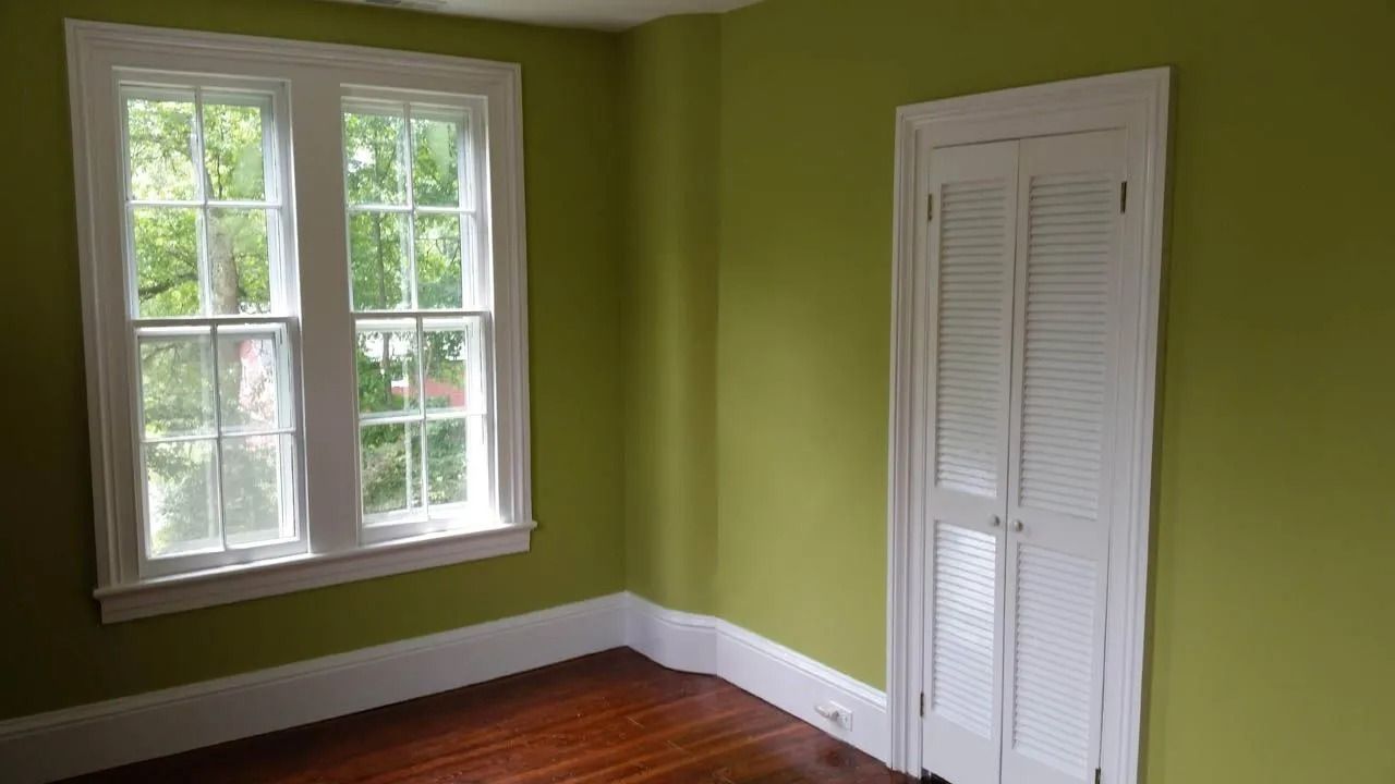 Room with green walls, white window and closet, and wooden floor.
