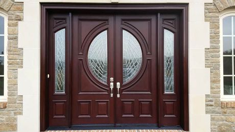 Dark brown double front doors with oval glass panels and sidelights, set in a stone facade.