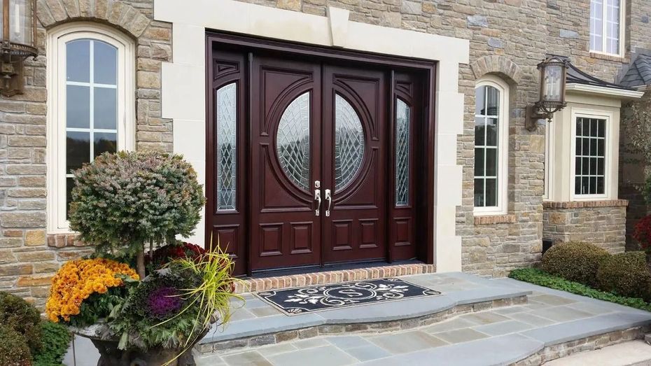 Brown double doors with oval glass and sidelights on a stone house facade.