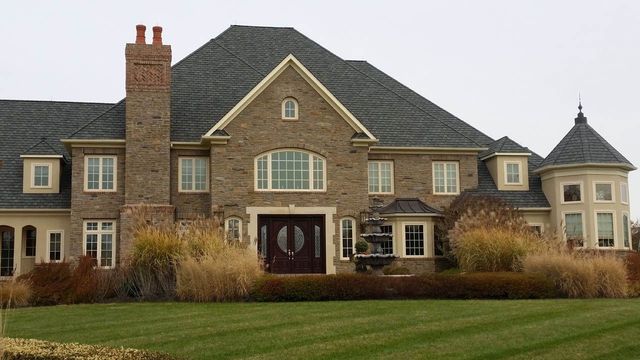 Large brick house with multiple windows, a tower, and a green lawn.