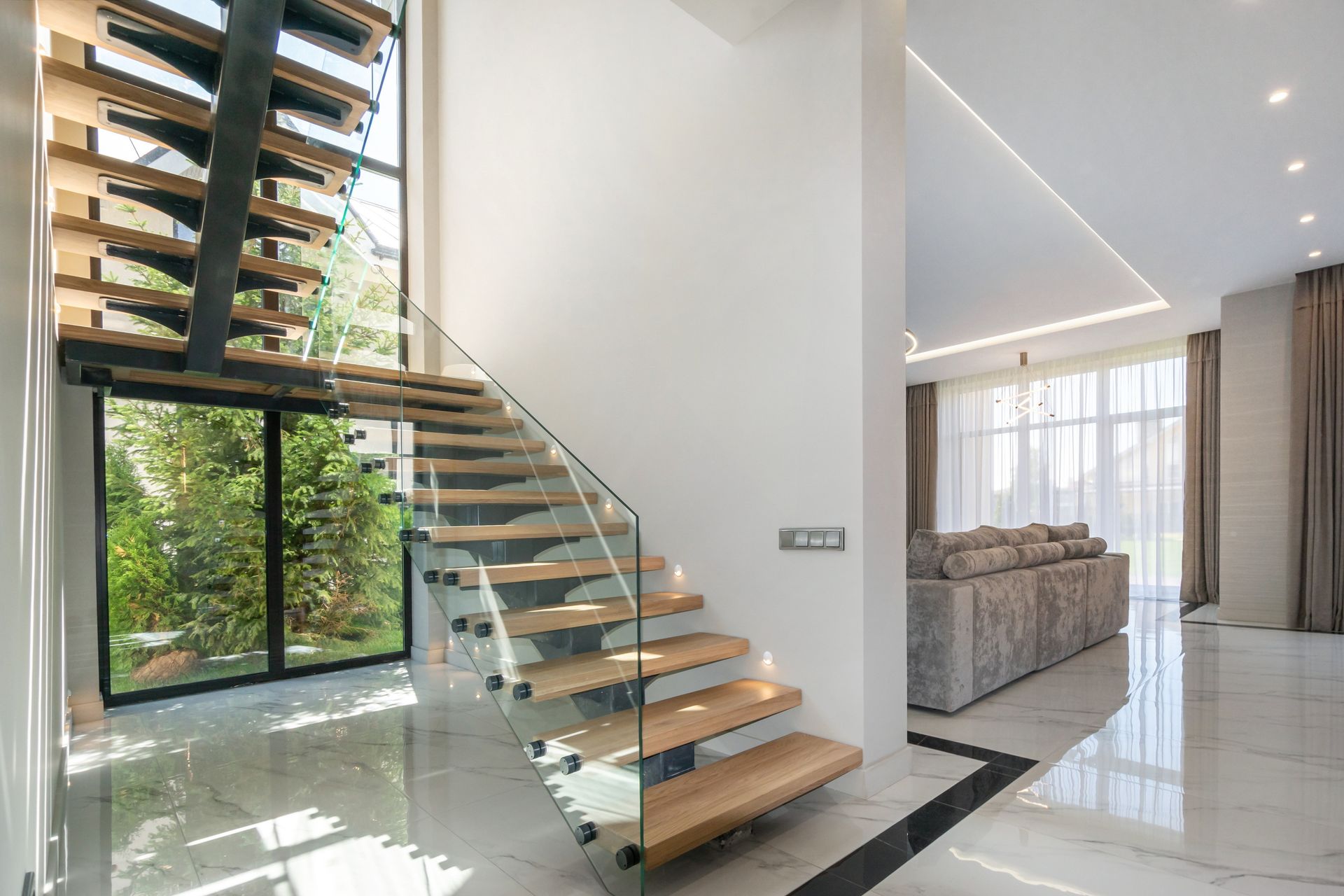 Modern luxury staircase with floating wood steps, glass railing, and bright open living area