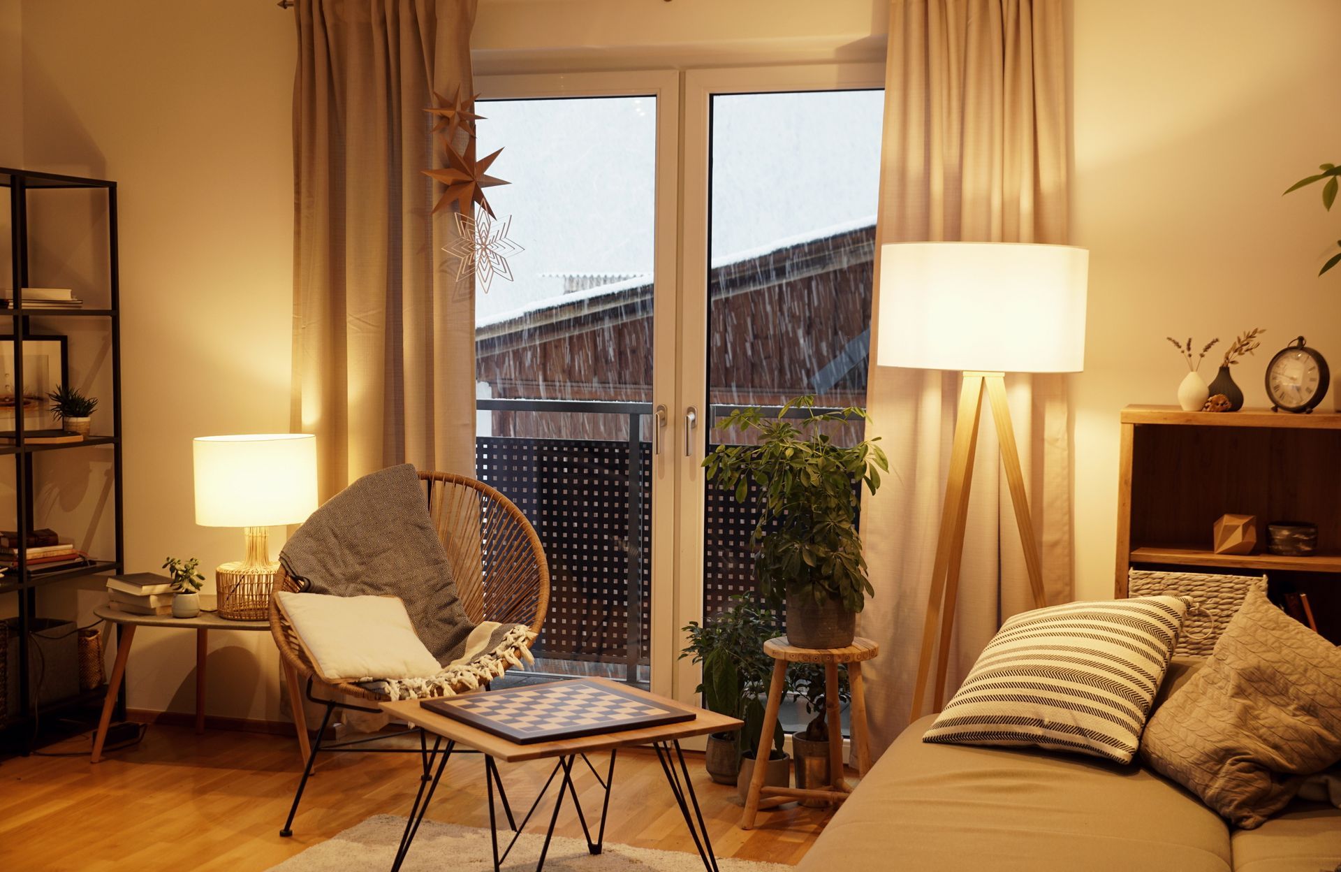 Cozy living room with warm lighting, sofa, chair, floor lamp, and glass doors to a balcony.