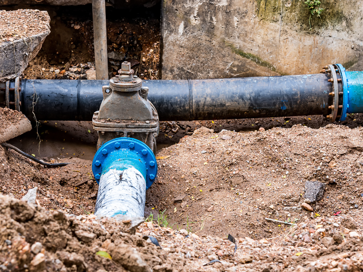 Water pipes in a trench, connected by a valve. Blue and black pipes in a dirt setting.