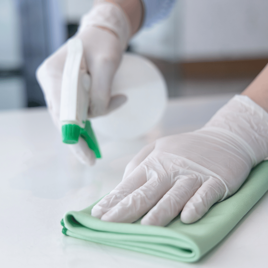 A person wearing white gloves is cleaning a table with a green cloth