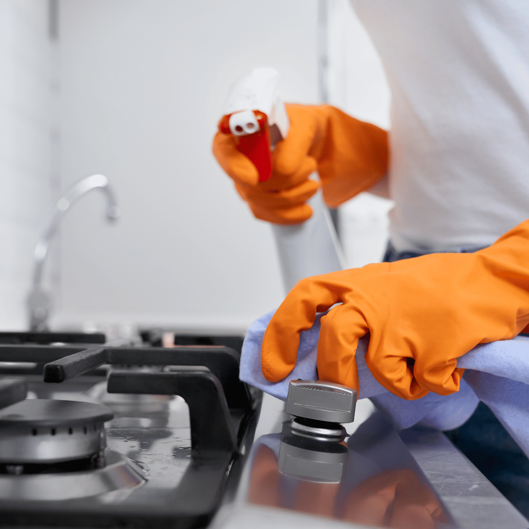 A person wearing orange gloves is cleaning a gas stove