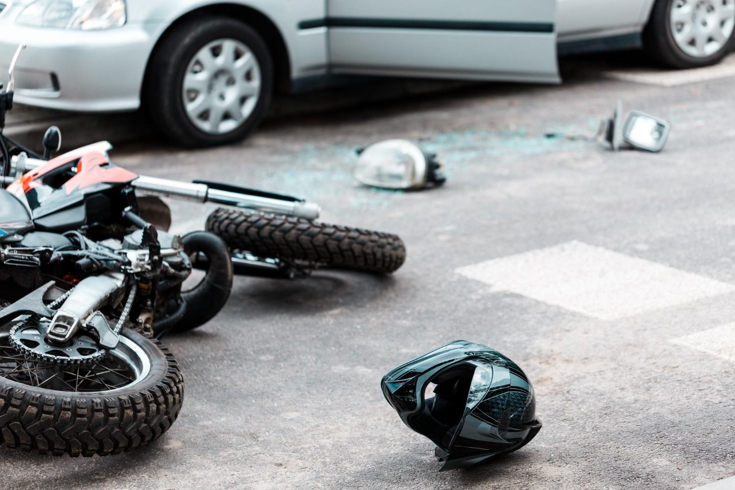 Motorcycle crash scene: motorcycle on ground, car with open door, scattered debris.