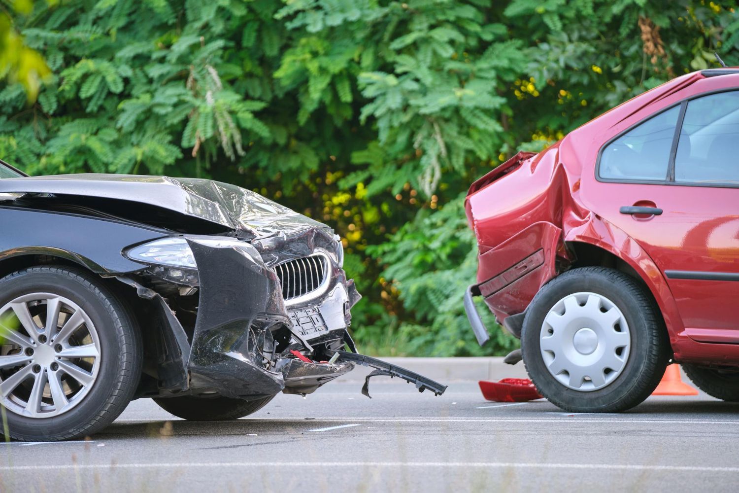 Cars crashed, black car front end damaged, red car rear damaged, roadside setting.