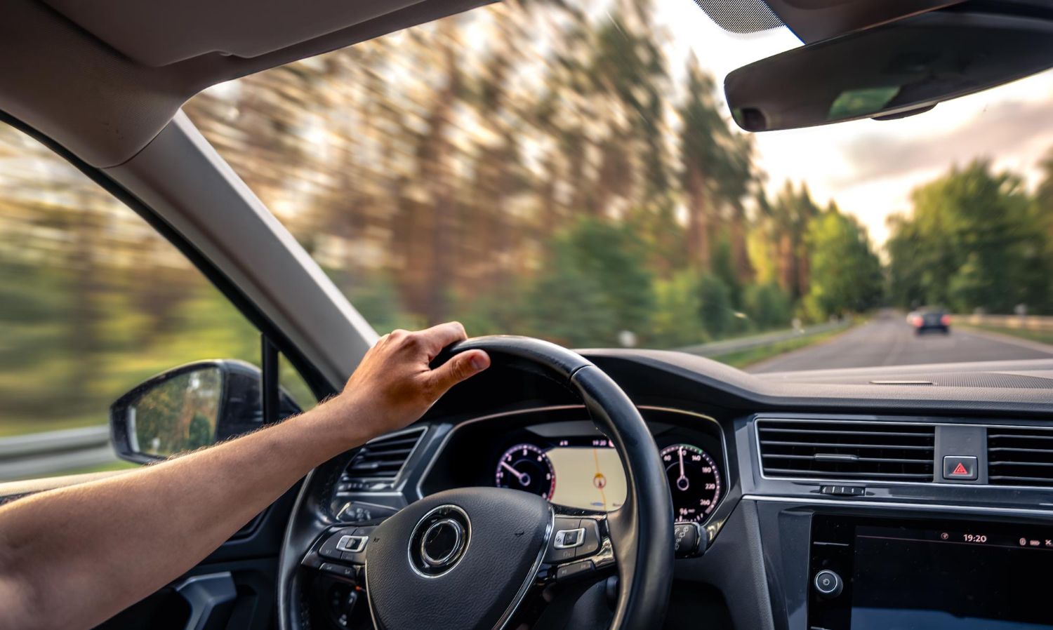 Hand on steering wheel driving on a road through a forest.