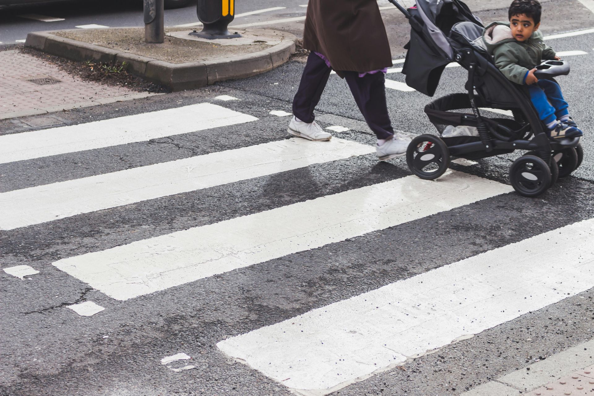 Person in hijab pushing a stroller with a child across a crosswalk.