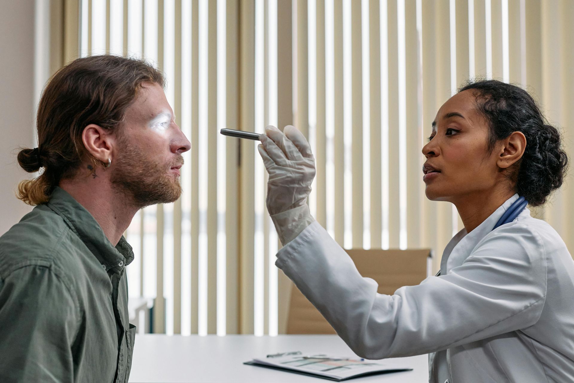 Doctor examining a patient's eye with a penlight in an office.