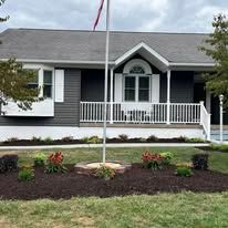 A house with a flag pole and a porch, surrounded by landscaping and a cloudy sky.