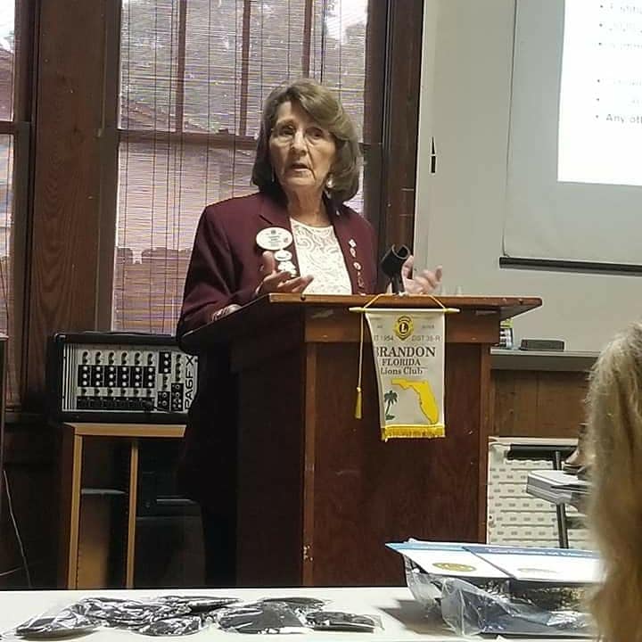 Woman speaking at a podium with a Lions Club banner, possibly giving a presentation.